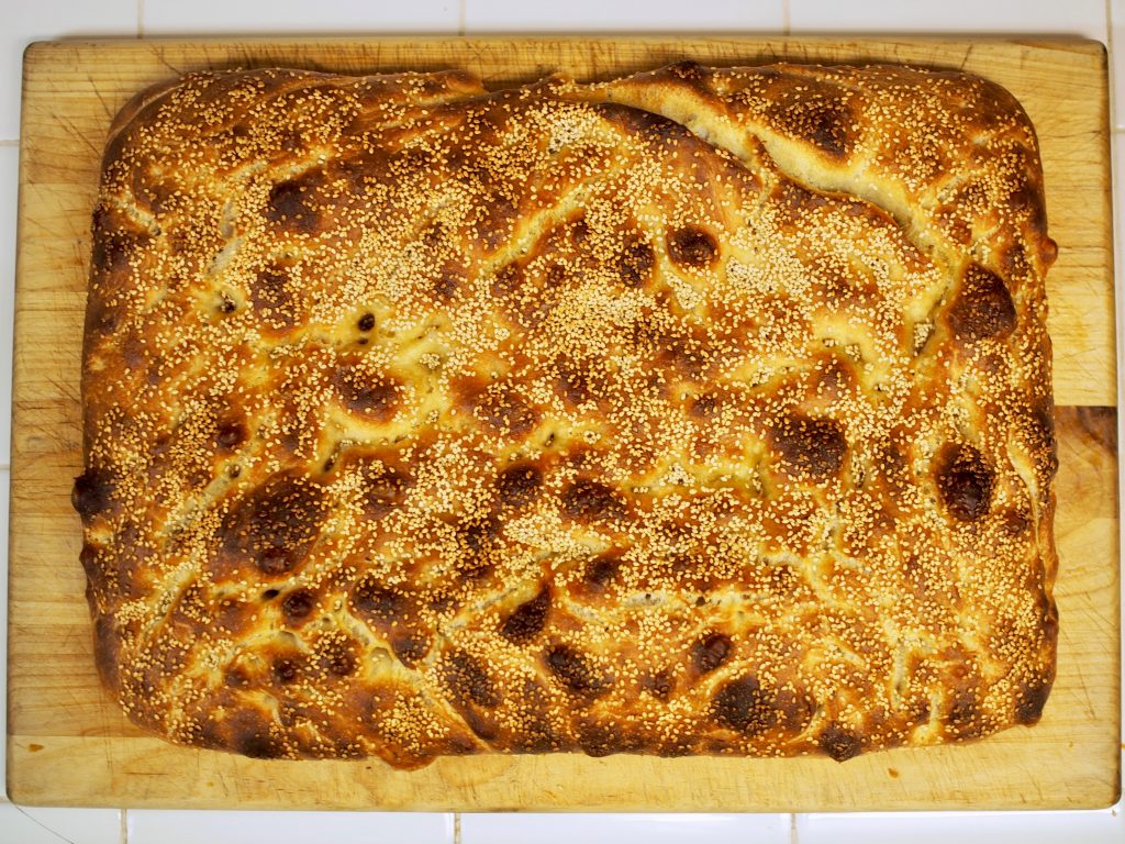 A browned focaccia ai semi di sesamo sits on cutting board.